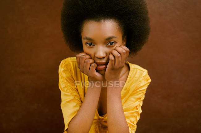 African-American woman in bright yellow dress looking at camera on brown background — Stock Photo