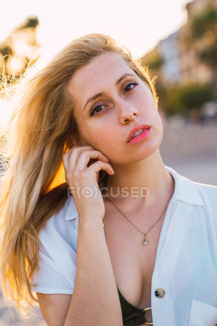 Блондинка, стоящая на улице под солнечным светом и смотрящая в камеру — стоковое фото