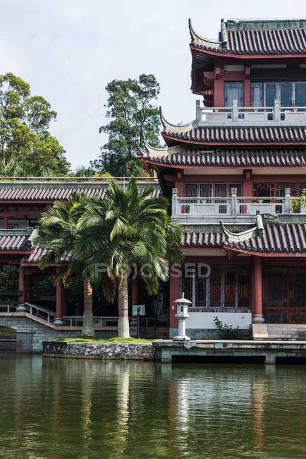 Extérieur du bâtiment traditionnel oriental avec palmiers tropicaux sur la côte du lac dans les montagnes Qingxiu, Nanning, Chine — Photo de stock