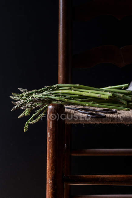 Nahaufnahme eines Bündels frischen grünen Spargels auf einem Stuhl auf schwarzem Hintergrund — Stockfoto