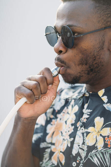 Uomo nero elegante con gli occhiali da sole. Sta vaporizzando con una sigaretta elettronica all'aperto — Foto stock