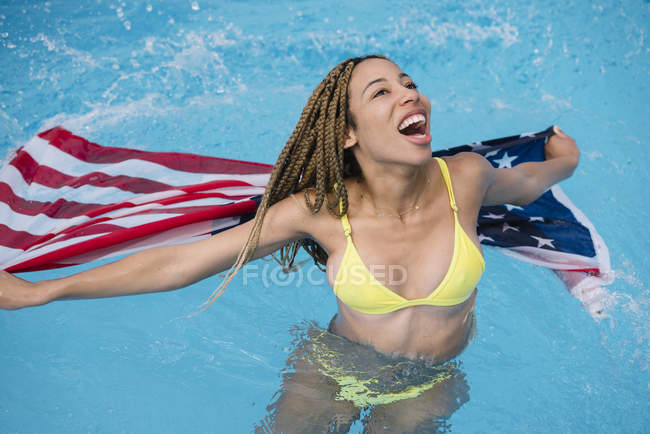 Feliz mujer emocionada divirtiéndose en la piscina con bandera americana - foto de stock