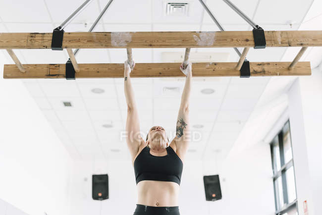 Strong woman in sportswear hanging on wooden board in gym and pulling up — Stock Photo