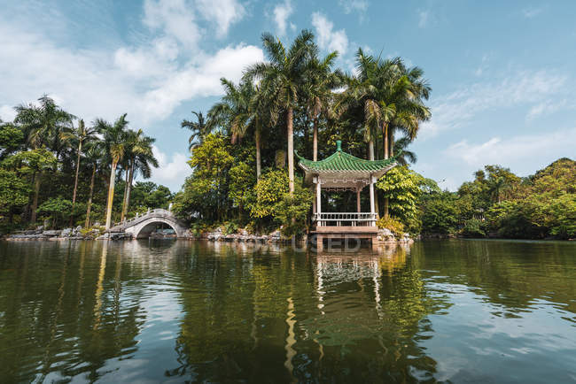 Oriental building on lake coast and stone bridge in tropical park, Nanning, China — Stock Photo