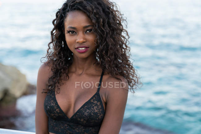 Charming black woman looking at camera in front of sea — Stock Photo