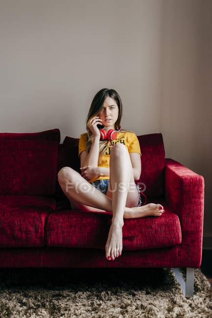 Женщина в наушниках сидит на диване и смотрит в камеру — стоковое фото