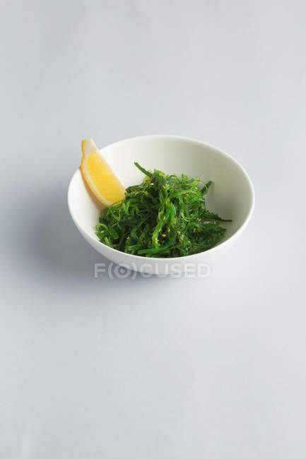 Japanese seaweed salad with lemon wedge in white bowl — Stock Photo