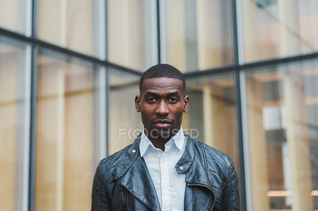 Black businessman in leather jacket standing against building — Stock Photo