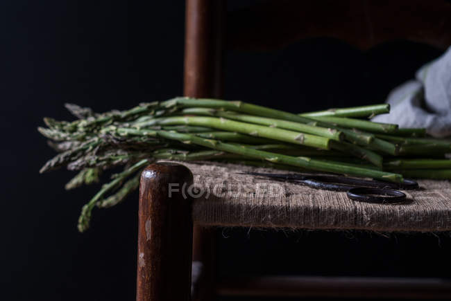 Close-up of bunch of fresh green asparagus on chair on black background — Stock Photo