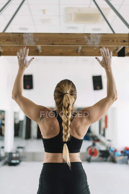 Rückansicht einer starken Frau in Sportbekleidung, die mit erhobenen Händen auf einem Holzbrett in der Turnhalle steht — Stockfoto