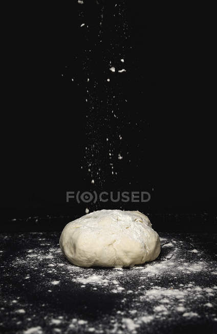 Massa em pó com farinha em mesa de cozinha sobre fundo preto — Fotografia de Stock