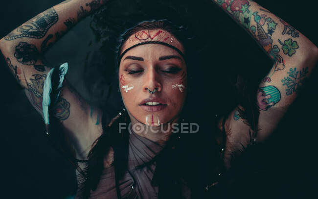 Atractiva joven con dibujos indios tradicionales en la cara relajante en el agua con los ojos cerrados - foto de stock