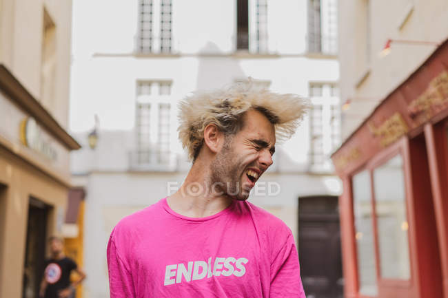 Homme élégant aux cheveux blonds et t-shirt rose posant sur la rue — Photo de stock