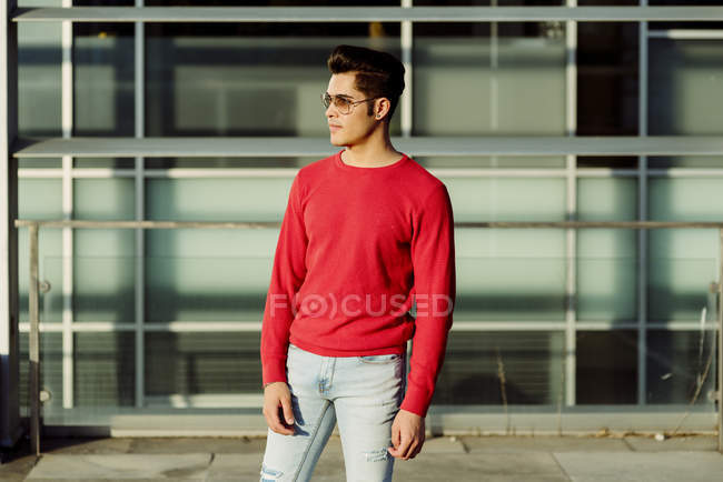 Atractivo joven de pie frente al edificio y mirando hacia otro lado - foto de stock
