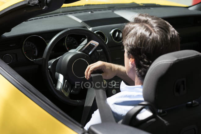Man fastening belt in modern yellow cabriolet — Stock Photo