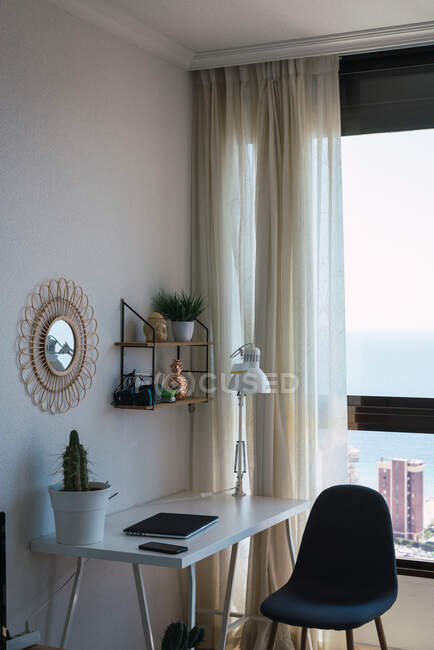 Various stuff standing on shelf and desk near huge window in cozy light room — Stock Photo