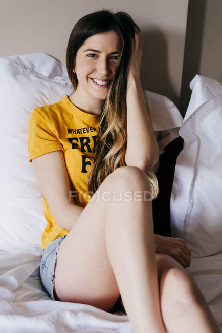 Hübsche lächelnde Frau, die auf dem Bett liegt und Haare berührt — Stockfoto