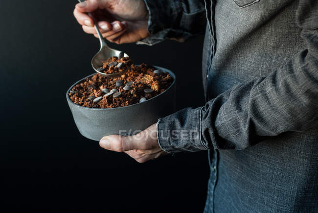 Manos masculinas sosteniendo tazón de granola de quinua crujiente sobre fondo oscuro - foto de stock