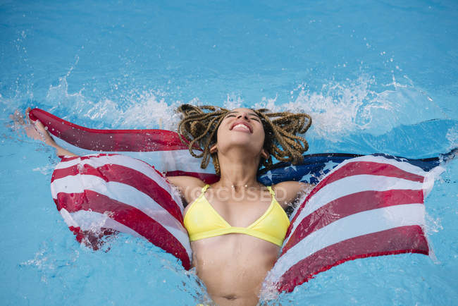 Relaxed smiling woman splashing in swimming pool with American flag — Stock Photo