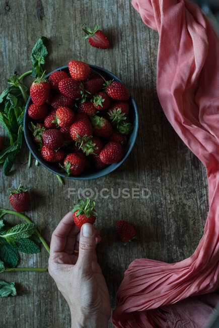 Hand taking delicious strawberry from bowl — Stock Photo