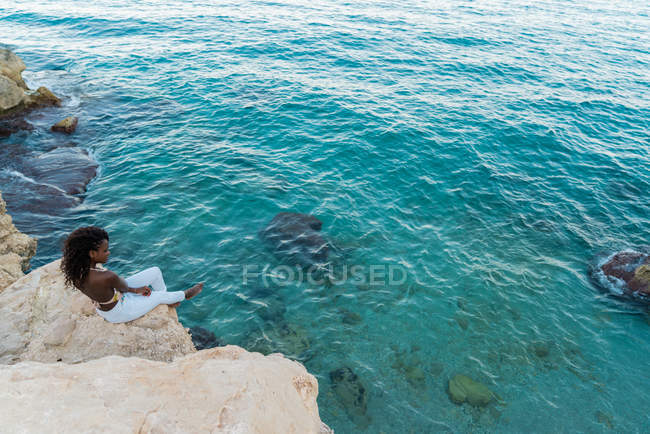 Mujer pensativa sentada en el acantilado sobre el agua cristalina turquesa - foto de stock