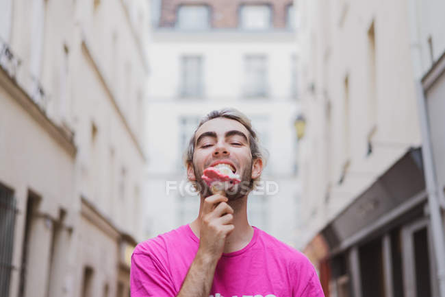 Elegante hombre de camiseta rosa comiendo helado en la calle - foto de stock