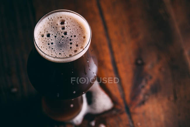 Толстое пиво в стекле на тёмном деревянном столе — стоковое фото