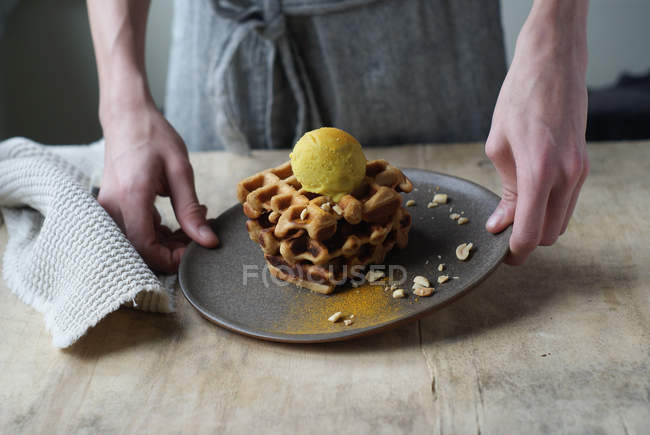 Human hands holding waffles with banana and curry ice cream on plate — Stock Photo