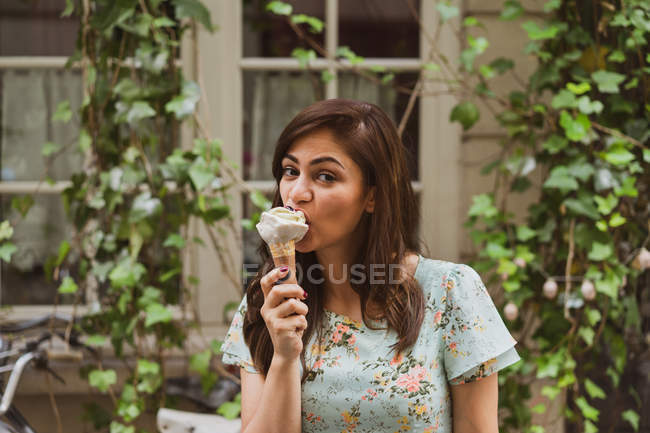 Молодая женщина держит мороженое перед окном с ползучим растением — стоковое фото