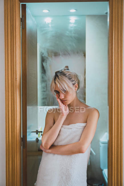 Jovem mulher envolto em toalha branca em pé na porta do banheiro após o chuveiro — Fotografia de Stock