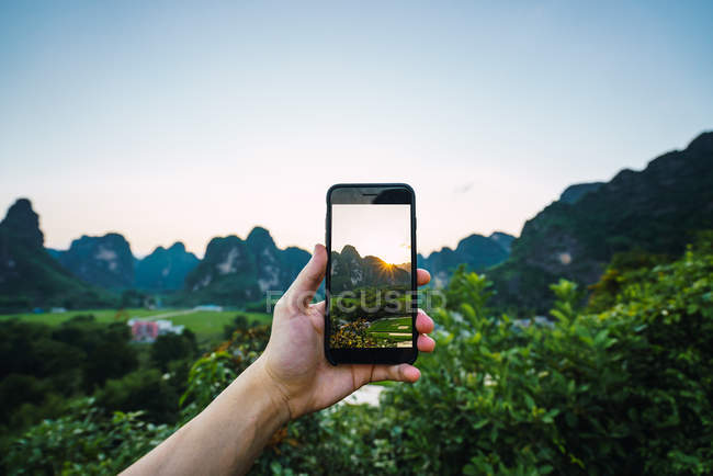Human hand taking picture with smartphone of green valley with mountains at sunset, Guangxi, China — Stock Photo
