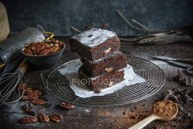 Pedaços de chocolate delicioso brownie o n rack de arame com ingredientes na superfície de madeira escura — Fotografia de Stock
