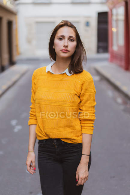 Hübsche Frau in gelber Strickjacke steht auf der Straße und schaut in die Kamera — Stockfoto