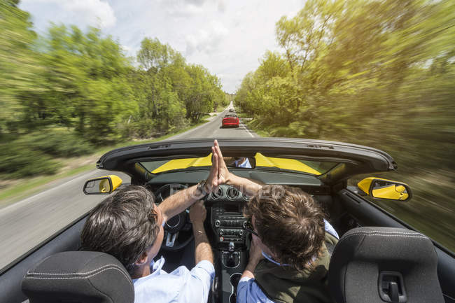 Чоловіки їздять на сучасній швидкій машині по дорозі в сільській місцевості — стокове фото