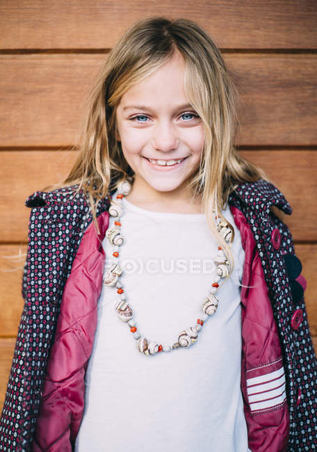 Ritratto di sorridente ragazza bionda con gli occhi azzurri in piedi sfondo di legno — Foto stock