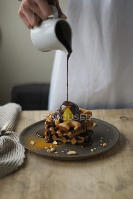 Человеческая рука льет шоколадный соус на вафли на тарелку — стоковое фото