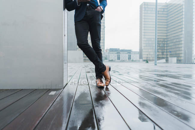 Pernas de homem de negócios inclinado na parede ao ar livre na chuva — Fotografia de Stock