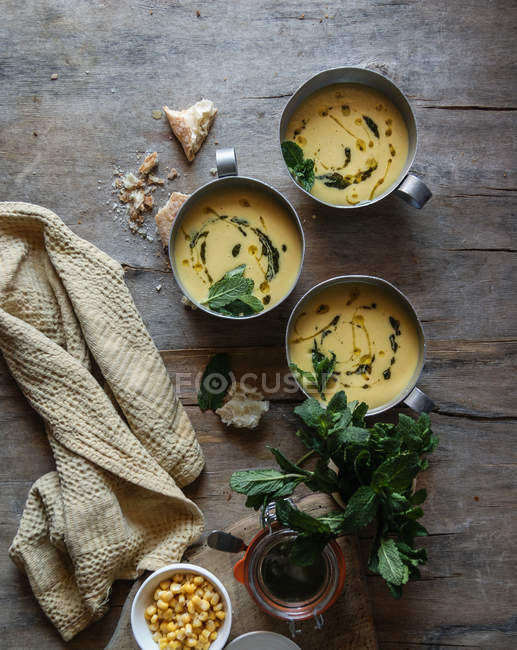 Sopa de creme de milho com coco e pesto em tigelas em mesa de madeira com ingredientes — Fotografia de Stock