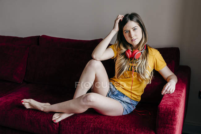 Женщина в наушниках сидит на диване и смотрит в камеру — стоковое фото
