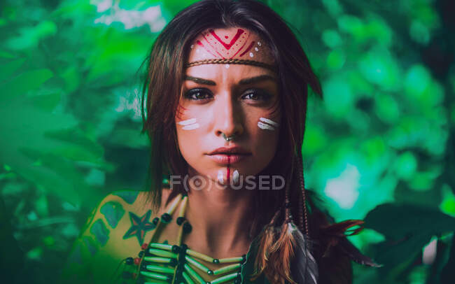 Привлекательная молодая женщина с традиционными индийскими картинами на лице, смотрящая в камеру и стоя в лесу — стоковое фото