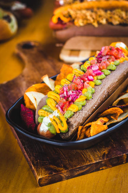 Primer plano de delicioso perrito caliente adornado con verduras y patatas fritas en el plato - foto de stock