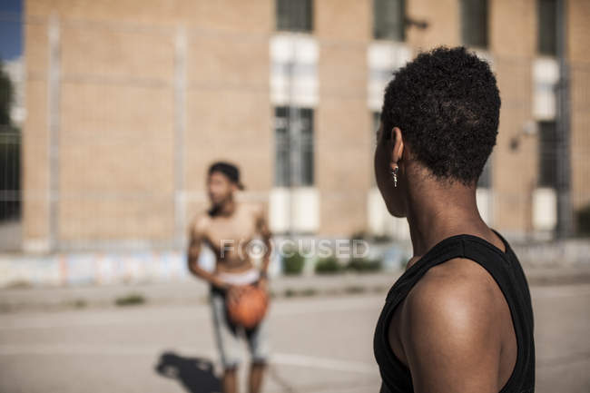 Young boy looking at brother playing basketball on court of neighborhood — Stock Photo