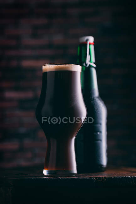 Stout beer in glass and bottle on wooden table on dark background — Stock Photo