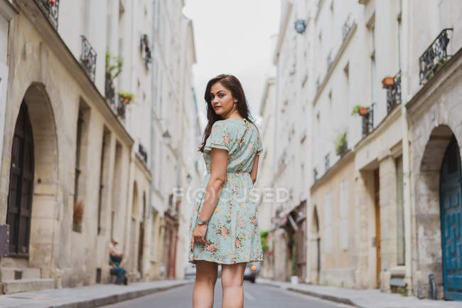 Visão traseira da jovem mulher em vestido de verão bonito com impressão floral andando na rua e olhando sobre o ombro — Fotografia de Stock