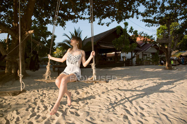 Jovem mulher sentada em balanços na praia de areia — Fotografia de Stock