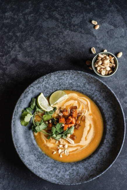 Thai-Kürbissuppe mit Limetten und Erdnüssen in grauem Teller auf grauer Oberfläche — Stockfoto