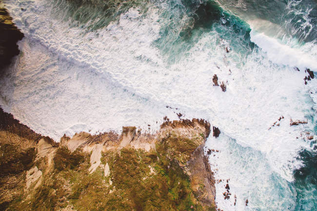 Морские волны с белой пеной катятся вверх по скалистому берегу в солнечный летний день — стоковое фото