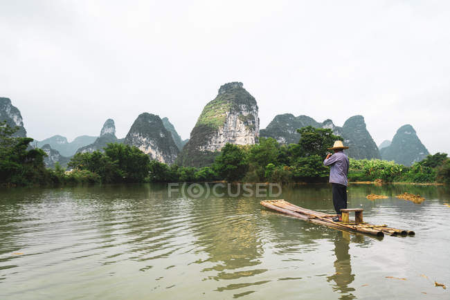 Chinois assis sur un radeau sur la rivière avec des montagnes pittoresques sur le fond, Guangxi, Chine — Photo de stock