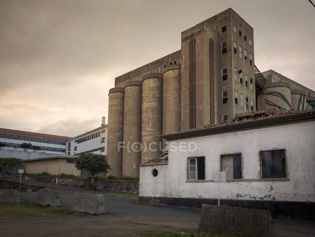 Schöne alte verwitterte Wände aus grauen Fabrikgebäuden und leere Straße im Sommer bei Sonnenuntergang — Stockfoto