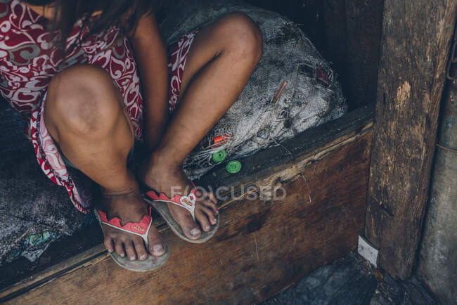 Crop shot from above of poor little girl sitting on weathered mattress in bad condition on wooden bed — Stock Photo